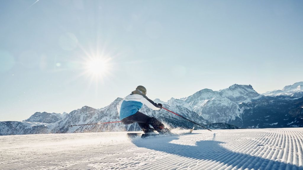Skier carving through fresh powder on a sunny day in the Dolomites, with majestic snow-capped mountains in the background.
