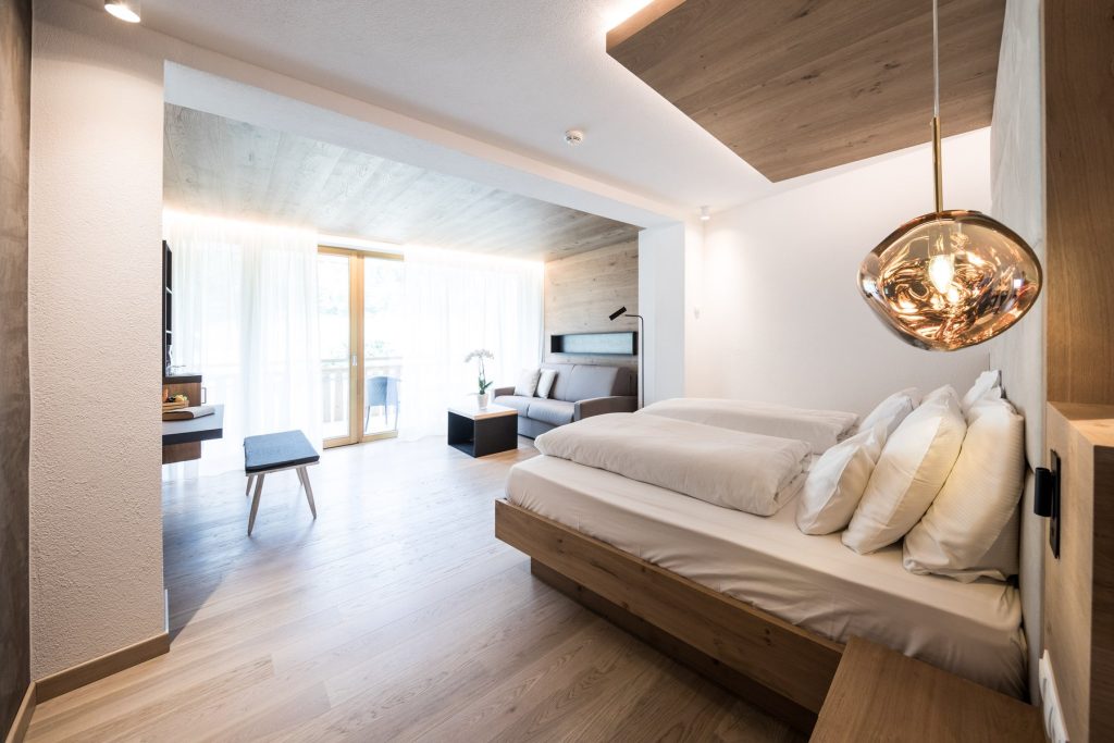Modern hotel room featuring wooden decor, a cozy seating area, large windows, and luxurious bedding.